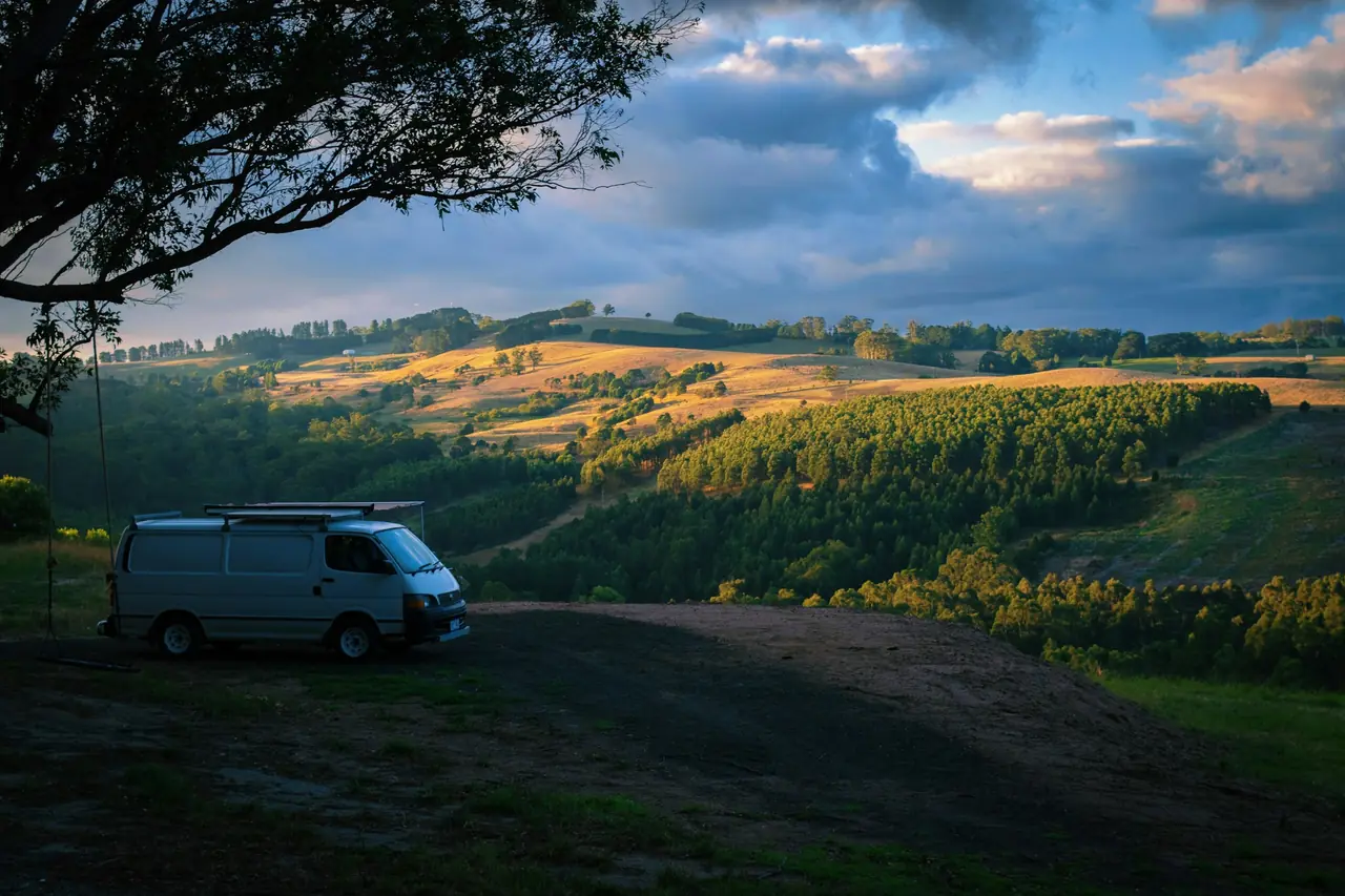 A campervan parked on a hilltop above farmland at sunset